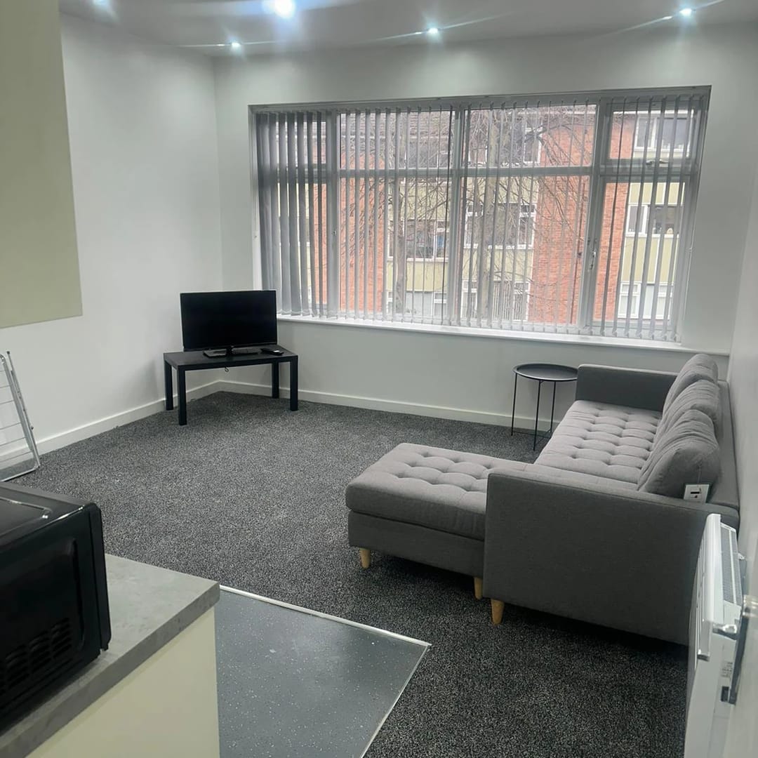 A furnished living room in one of our apartments, with a grey sofa and a large window
